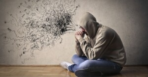 パーカー姿の男性が頭を抱える。思考ぐせによる混乱と人生の停滞を表現するイラスト