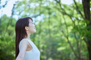 目を閉じ深呼吸する女性。仕事の苦痛から解放され、自然の中でリフレッシュするイメージ